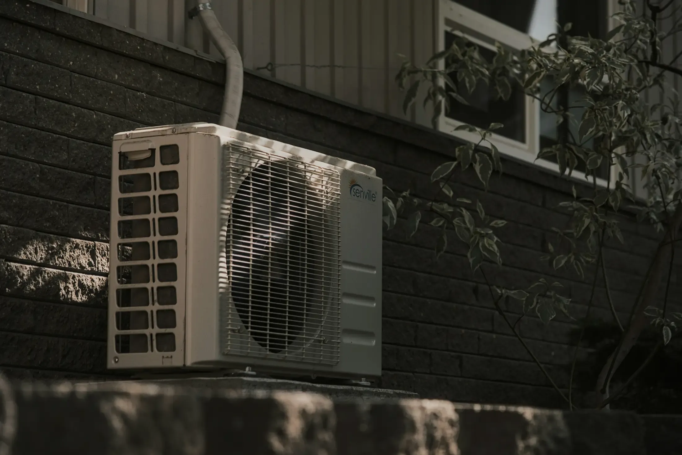 Outdoor condenser unit of a residential ductless mini-split air conditioning system, mounted on an exterior wall