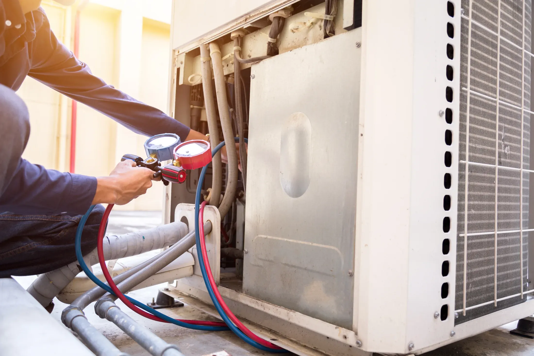 HVAC technician using gauges to measure refrigerant charge on an outdoor AC unit